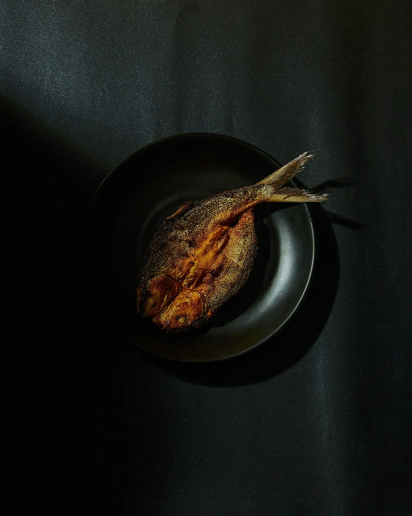 검은 접시 위 노릇하게 구운 참조기 한 마리